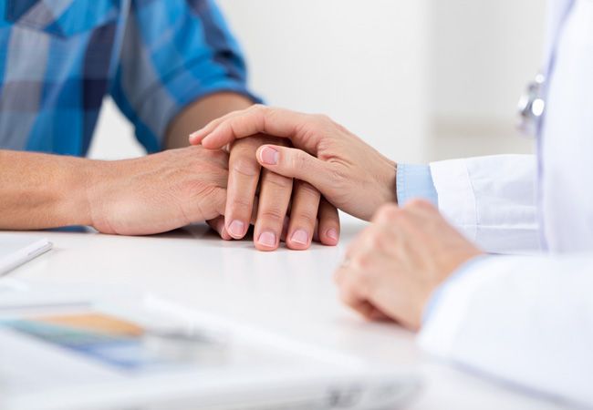 Врач в белом халате с стетоскопом мягко кладёт свою руку поверх руки пациента